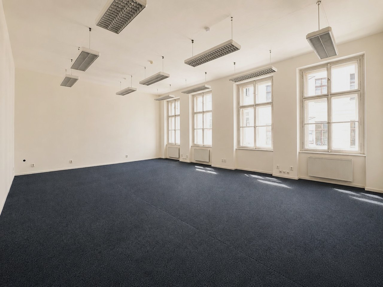 Open-space kancelária s vysokými oknami a tmavomodrým kobercom